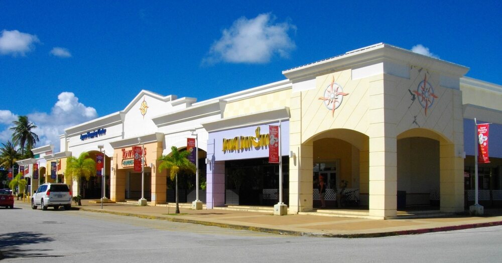 A multi-tenant shopping centre with arcaded storefronts, palms and banner signage