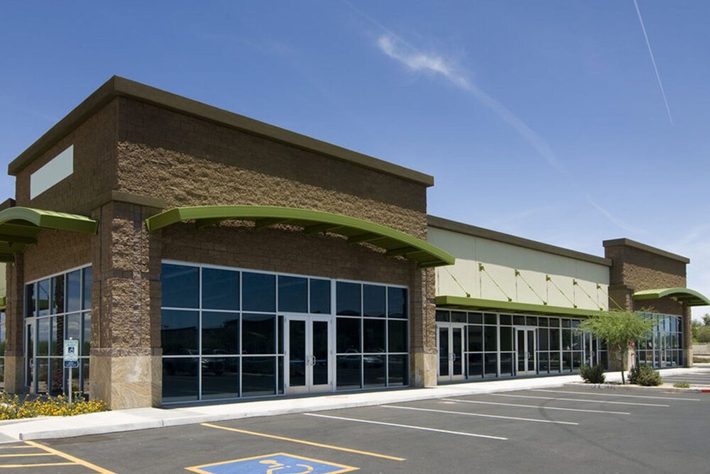 A completed multi-tenant retail strip centre with glass storefronts and surface parking